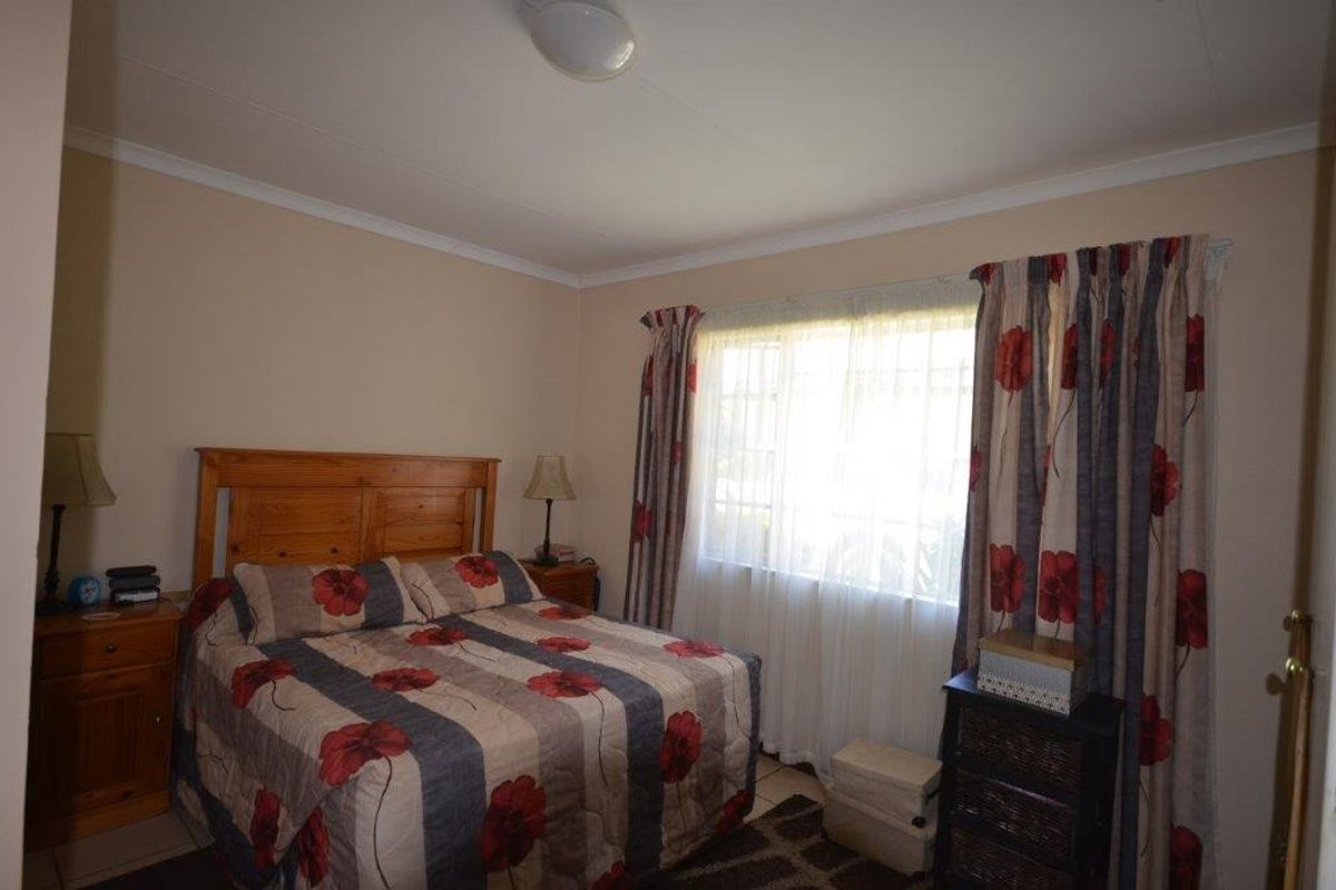 A comfortable bedroom featuring tiled flooring, neutral wall tones, and a large window allowing for natural light.