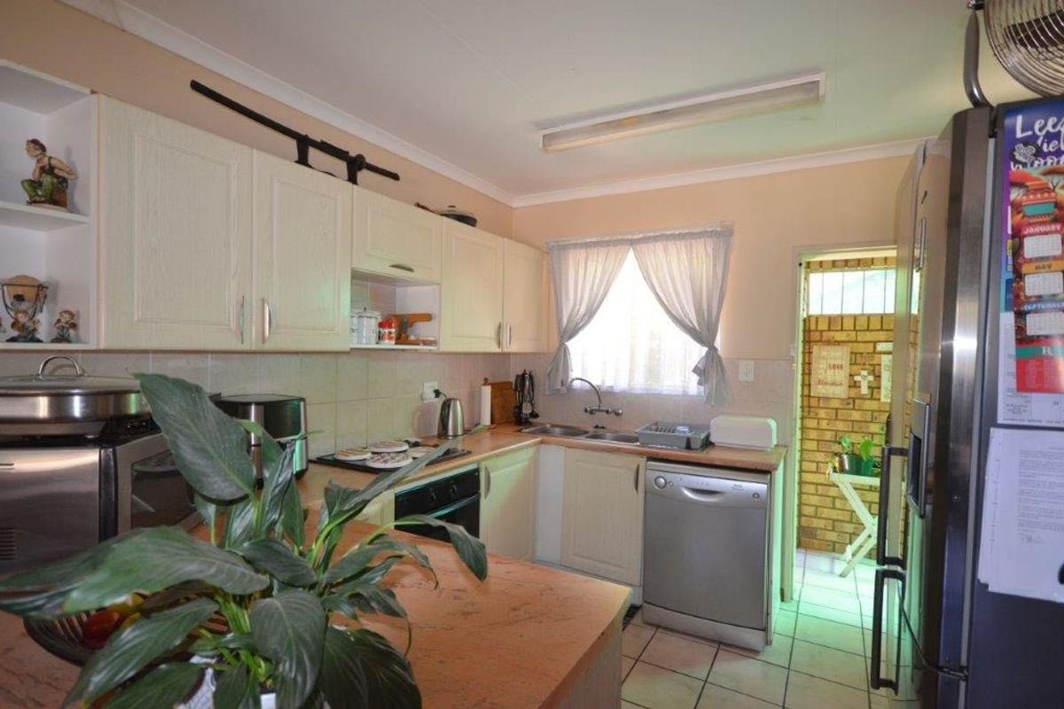 A functional kitchen featuring light-toned cabinetry, tiled splashbacks, a double sink, and direct access to an adjacent utility area.
