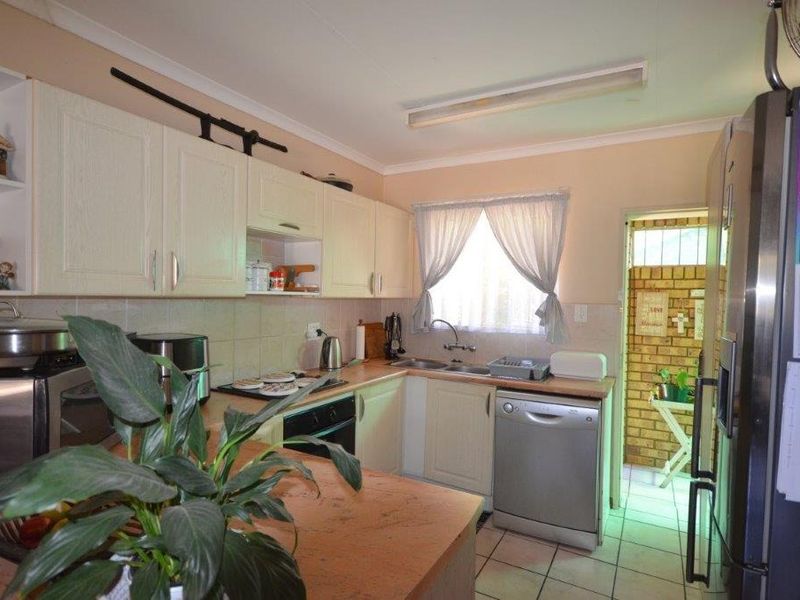 A functional kitchen featuring built-in cabinetry, laminate countertops, a stainless steel sink, and tiled flooring, with direct access to an adjacent utility area.