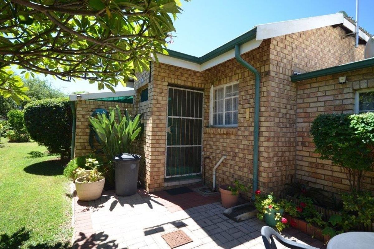 A view of the rear exterior featuring a face brick facade, paved patio area, and secure entrance gate within a well-maintained garden setting.