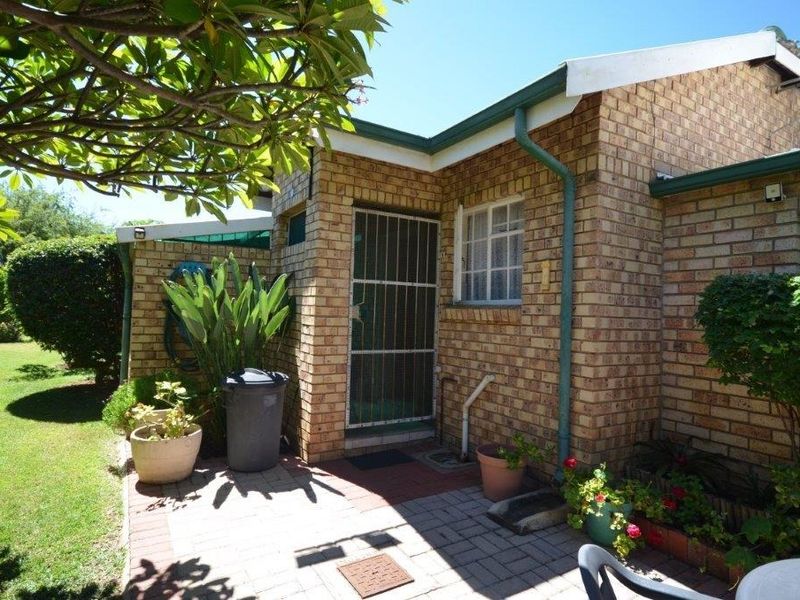A view of the rear exterior featuring a face brick facade, paved patio area, and secure entrance gate within a well-maintained garden setting.