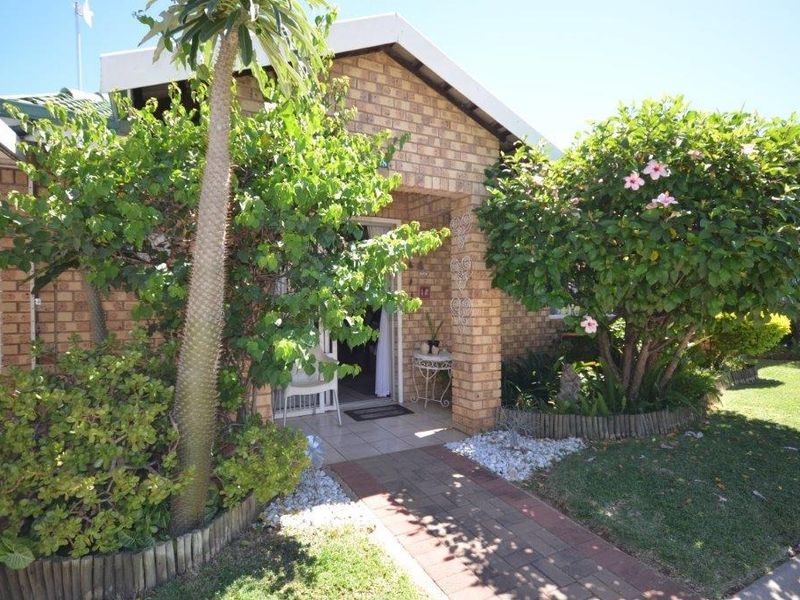 Front entrance of a retirement village unit featuring a brick facade, tiled porch, and a well-maintained landscaped garden with a paved walkway.