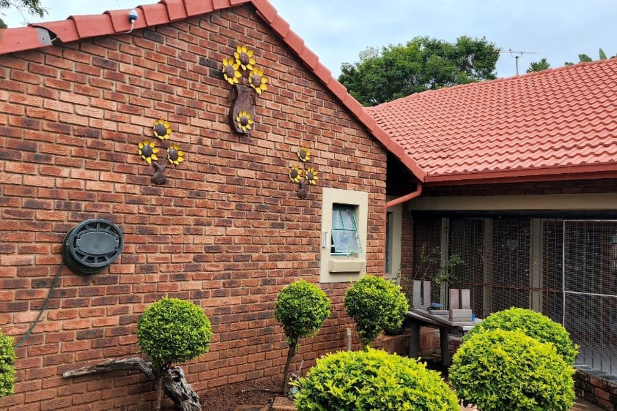 Rear exterior view of the property featuring face brick walls, terracotta roof tiles, and a secure enclosed patio area.