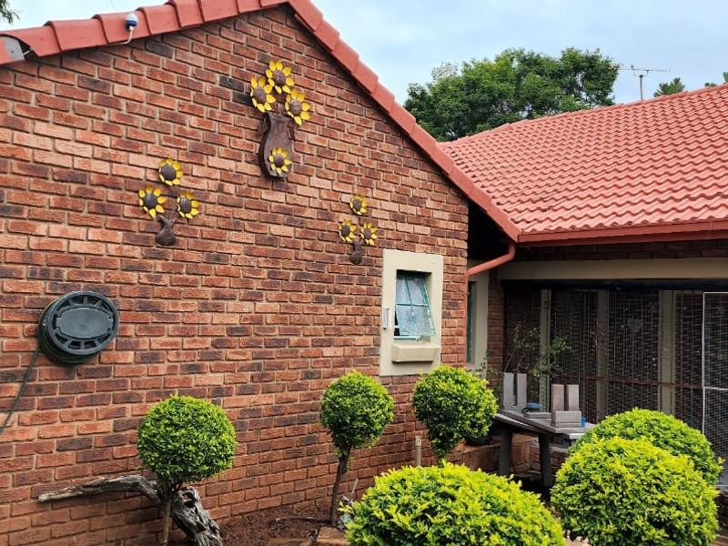 Rear exterior view of the property featuring face brick walls, terracotta roof tiles, and a secure enclosed patio area.