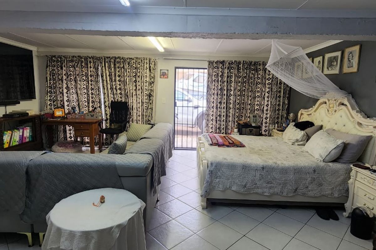 Spacious bedroom featuring tiled flooring, an exposed ceiling beam, and direct access to the exterior via a security gate.