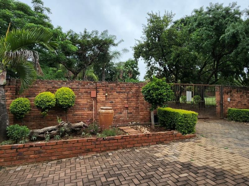 A well-maintained front exterior featuring a brick boundary wall, paved driveway, and established garden landscaping with secure gated access.