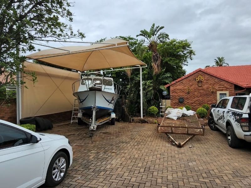 A paved rear driveway area featuring a shade sail structure, brick exterior walls, and tiled roofing.