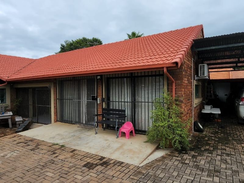 Front view of a face brick house featuring a tiled roof, paved driveway, and a covered carport area.