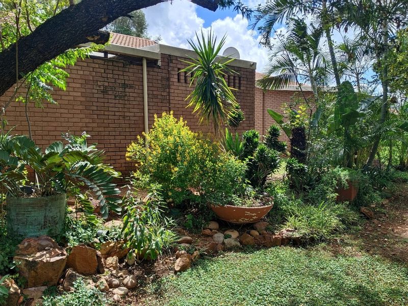 A view of the rear exterior brick wall and tiled roof, surrounded by established garden landscaping and mature trees.