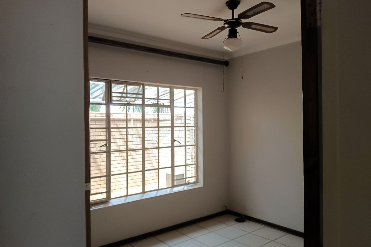 An empty bedroom featuring tiled flooring, a ceiling fan, and a window fitted with security bars.