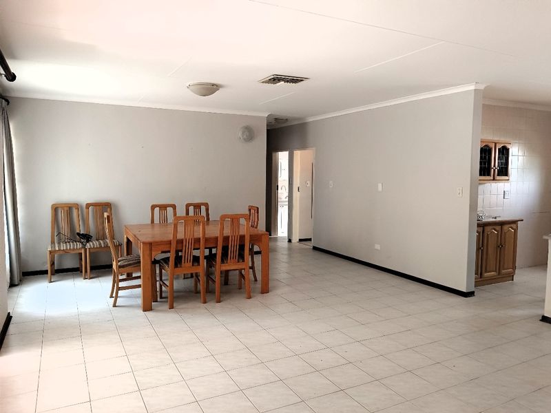 Spacious open-plan living and dining area featuring neutral tiled flooring, coved cornicing, and a semi-open kitchen with traditional timber cabinetry.