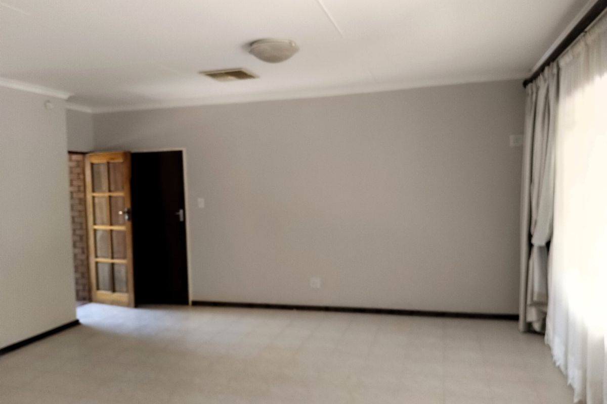A spacious, empty living area featuring neutral wall tones, tiled flooring, and a timber-framed door leading to an adjacent space.