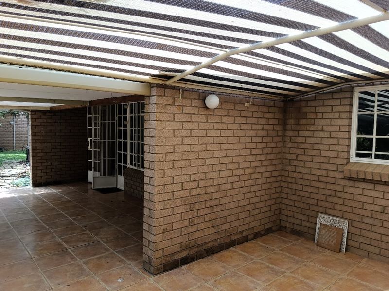 A covered outdoor patio area featuring brick walls, tiled flooring, and a striped shade cloth awning, providing a functional space for outdoor relaxation.