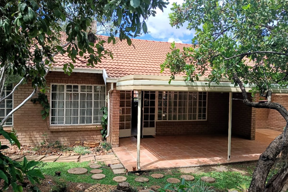 Rear view of the retirement unit featuring a covered tiled patio, brick exterior, and established garden surroundings.