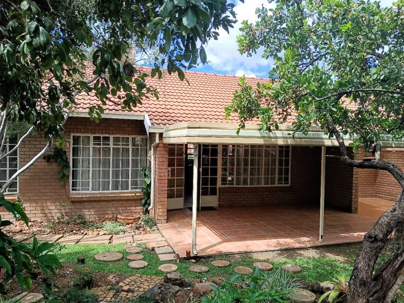 Rear view of the retirement unit featuring a covered tiled patio, brick exterior, and established garden surroundings.