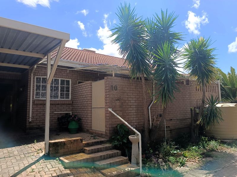 Front elevation of a brick retirement unit featuring a carport, paved entrance steps with a handrail, and an adjacent water tank.