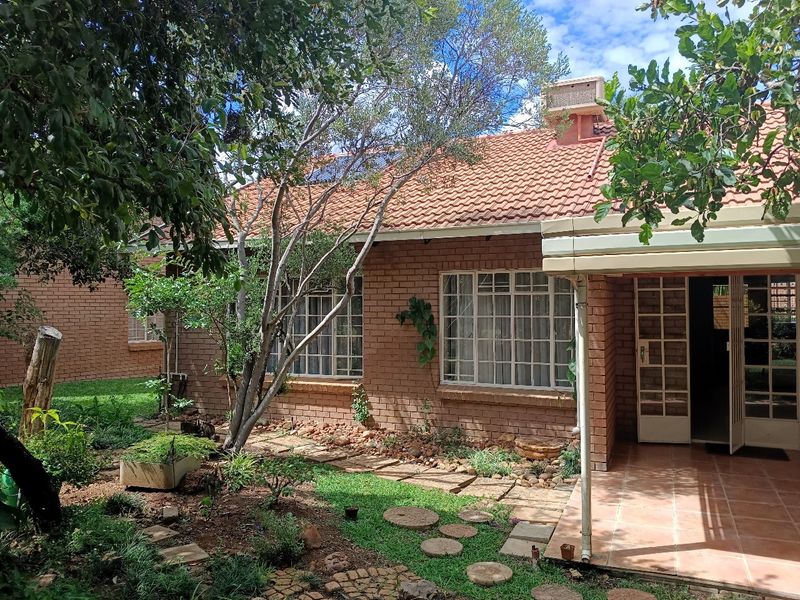 Rear view of a retirement village unit featuring a brick facade, terracotta roof tiles, and a covered tiled patio area overlooking a garden.