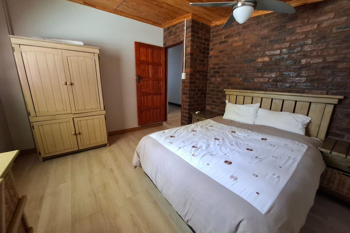 A bedroom featuring an exposed brick feature wall, timber ceiling, ceiling fan, and light-toned laminate flooring.