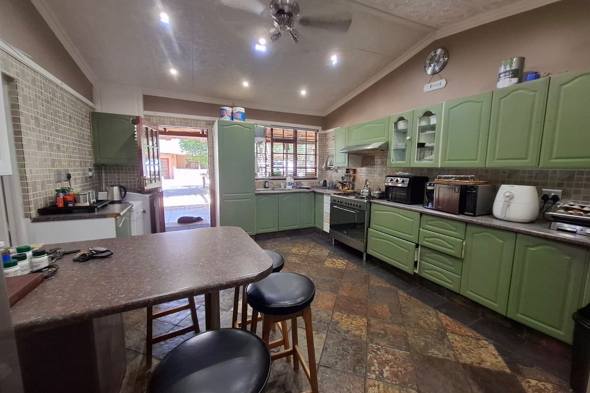 Spacious kitchen featuring green cabinetry, stone-look floor tiles, a built-in stove with extractor fan, and a breakfast counter with direct outdoor access.