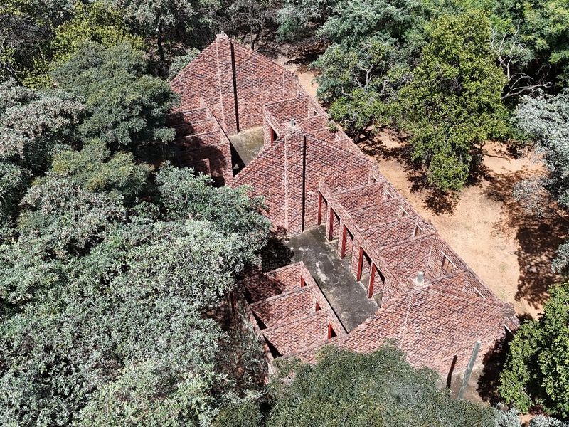 Aerial view of an incomplete brick building structure situated within a wooded small holding, showing only the masonry walls and concrete foundation.