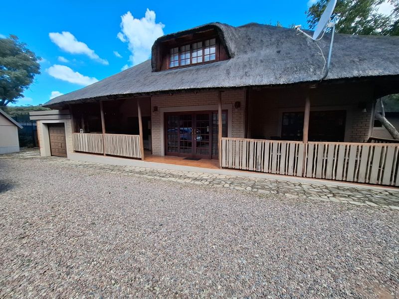 Front elevation of a thatch-roofed small holding property featuring a covered patio, brick facade, and attached garage with a gravel driveway.