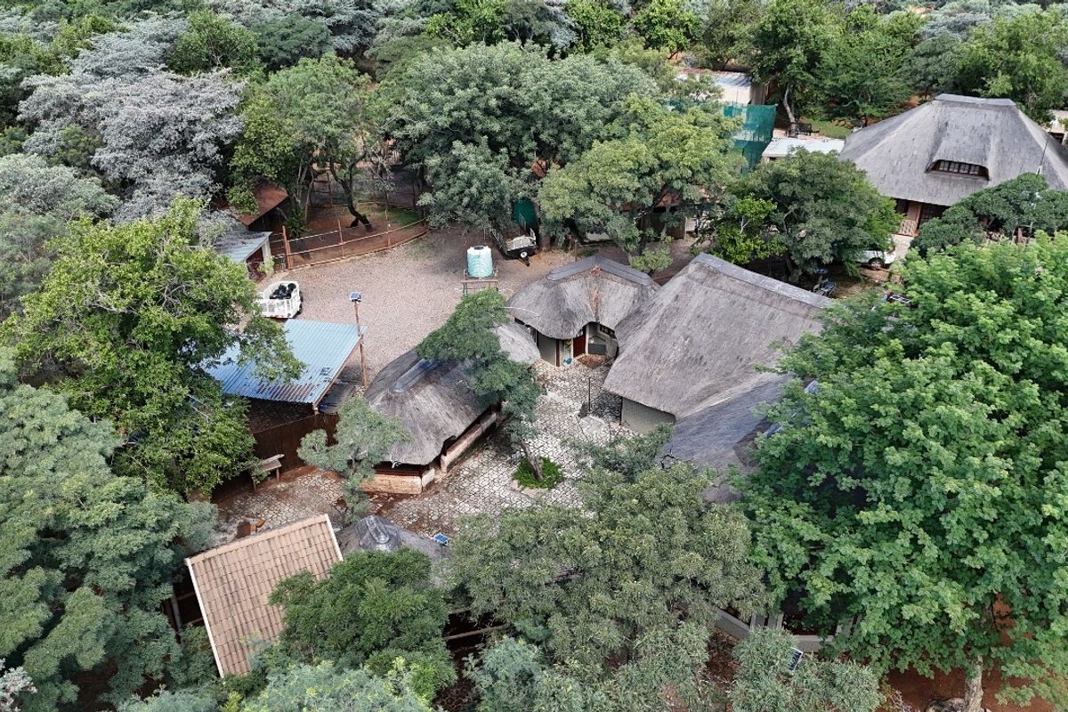 Aerial view of a small holding property featuring multiple thatched-roof buildings, a central paved courtyard, and extensive mature tree cover.