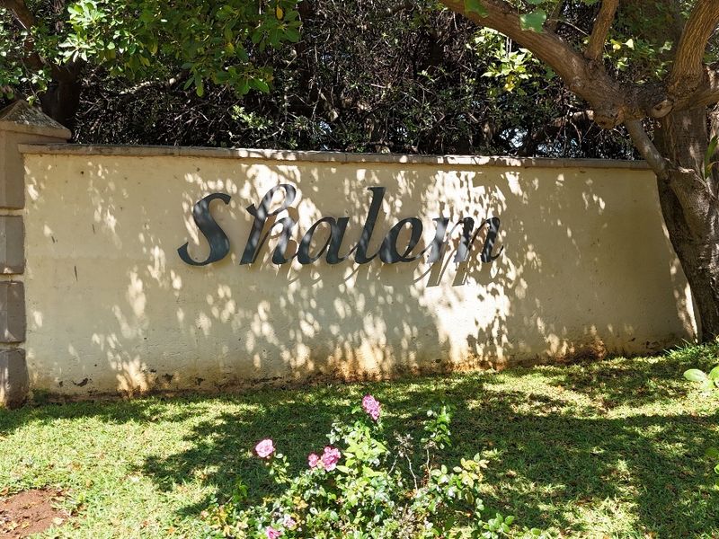 A view of the estate boundary wall featuring the property name signage, surrounded by established trees and garden landscaping.