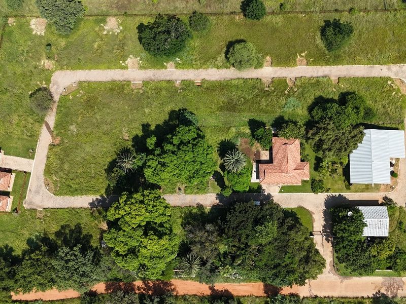 Aerial view of a residential property featuring multiple structures, extensive green space, mature trees, and a paved driveway layout.