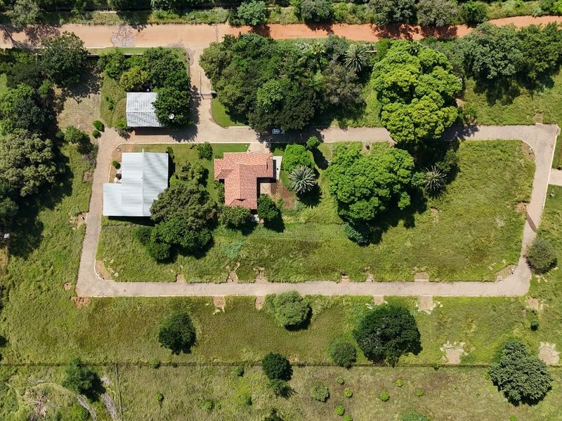 Aerial view of a residential property featuring established trees, paved driveway access, and existing structures on a large plot of land.