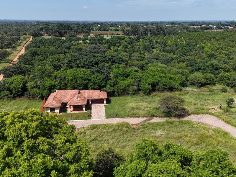Aerial view of a residential property featuring a tiled roof dwelling, paved driveway, and expansive surrounding green space and mature trees.