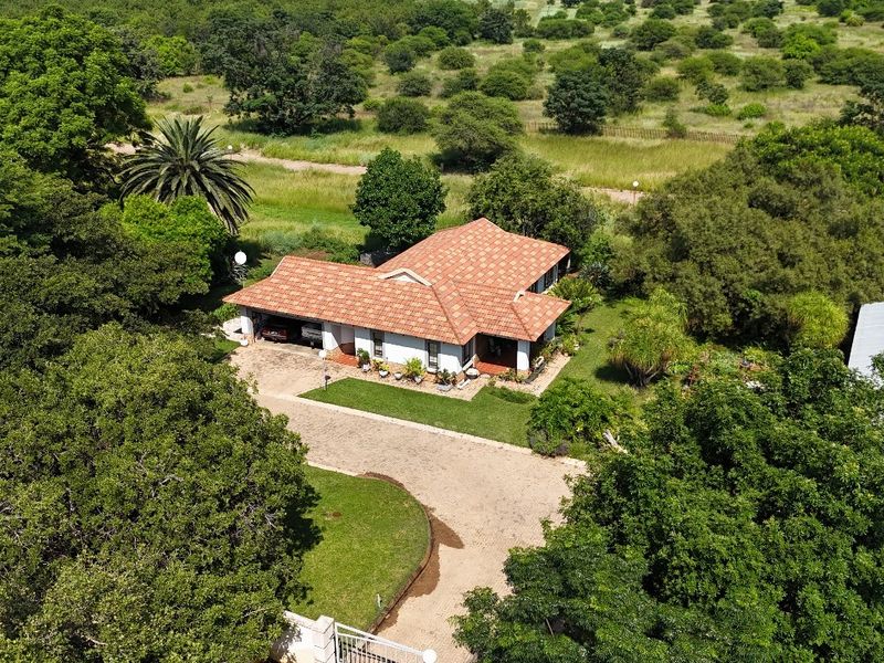 Aerial view of a residential property featuring a tiled roof home, paved driveway, and established garden surroundings in a spacious setting.