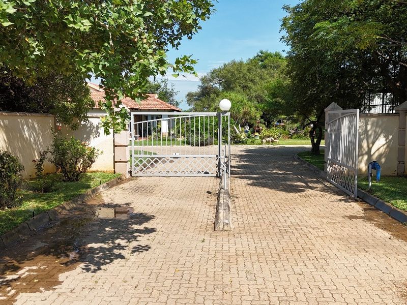 A gated residential entrance featuring a paved driveway, perimeter walls, and metal security gates leading into the property grounds.