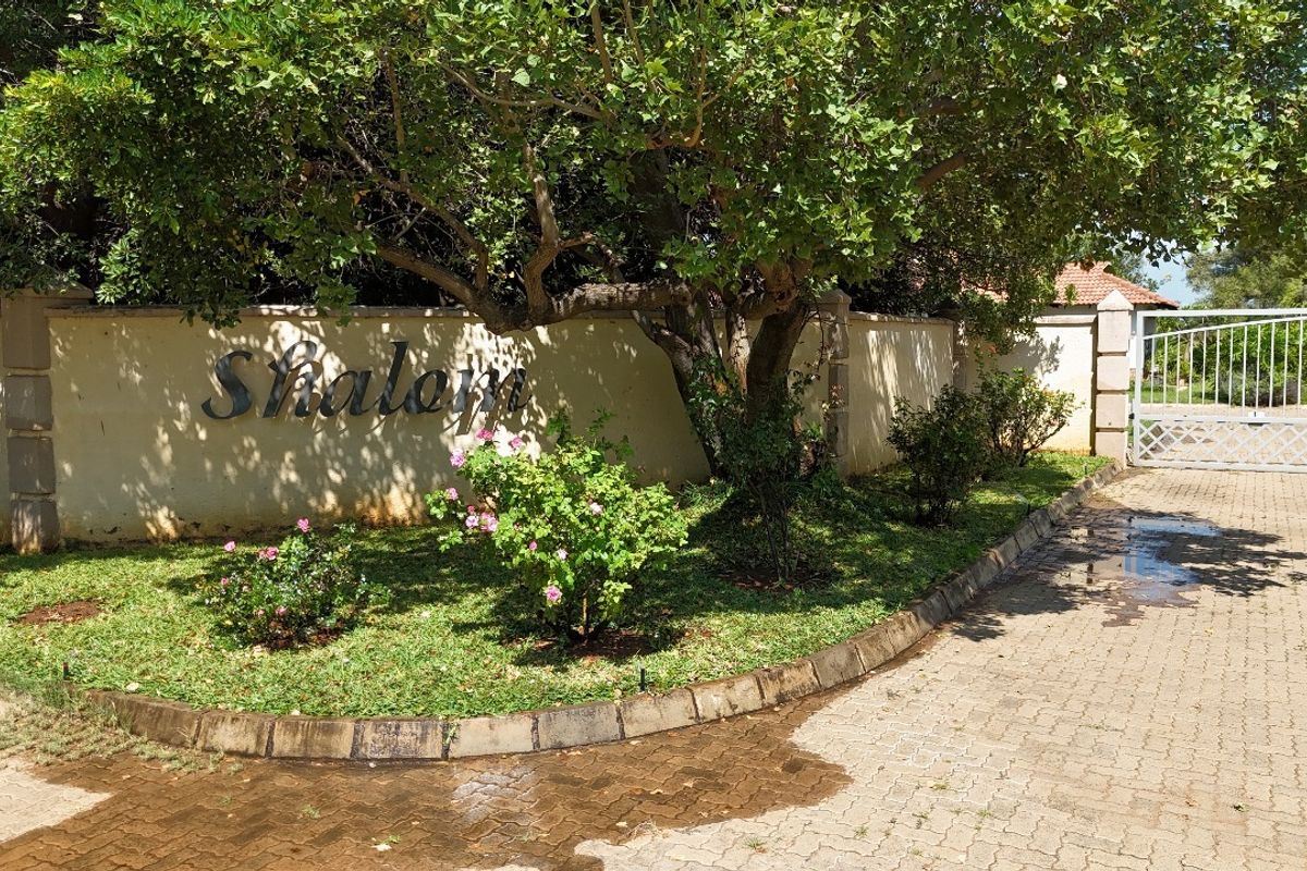 Front entrance view of the property featuring a paved driveway, boundary wall with signage, and established garden landscaping.