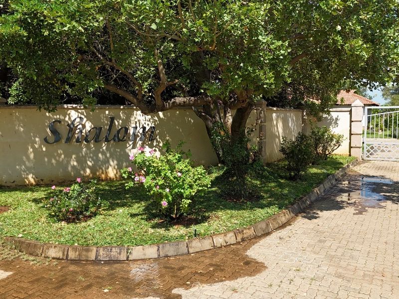 Front entrance view of the property featuring a paved driveway, boundary wall with signage, and established garden landscaping.