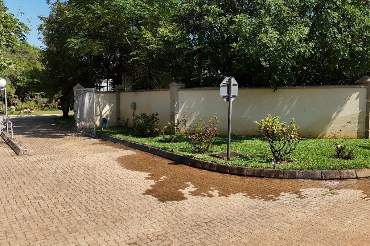 Front entrance area featuring a paved driveway, perimeter wall, and metal gate access to the property.