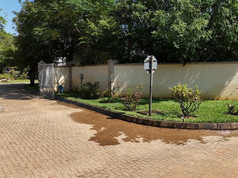 Front entrance area featuring a paved driveway, perimeter wall, and metal gate access to the property.