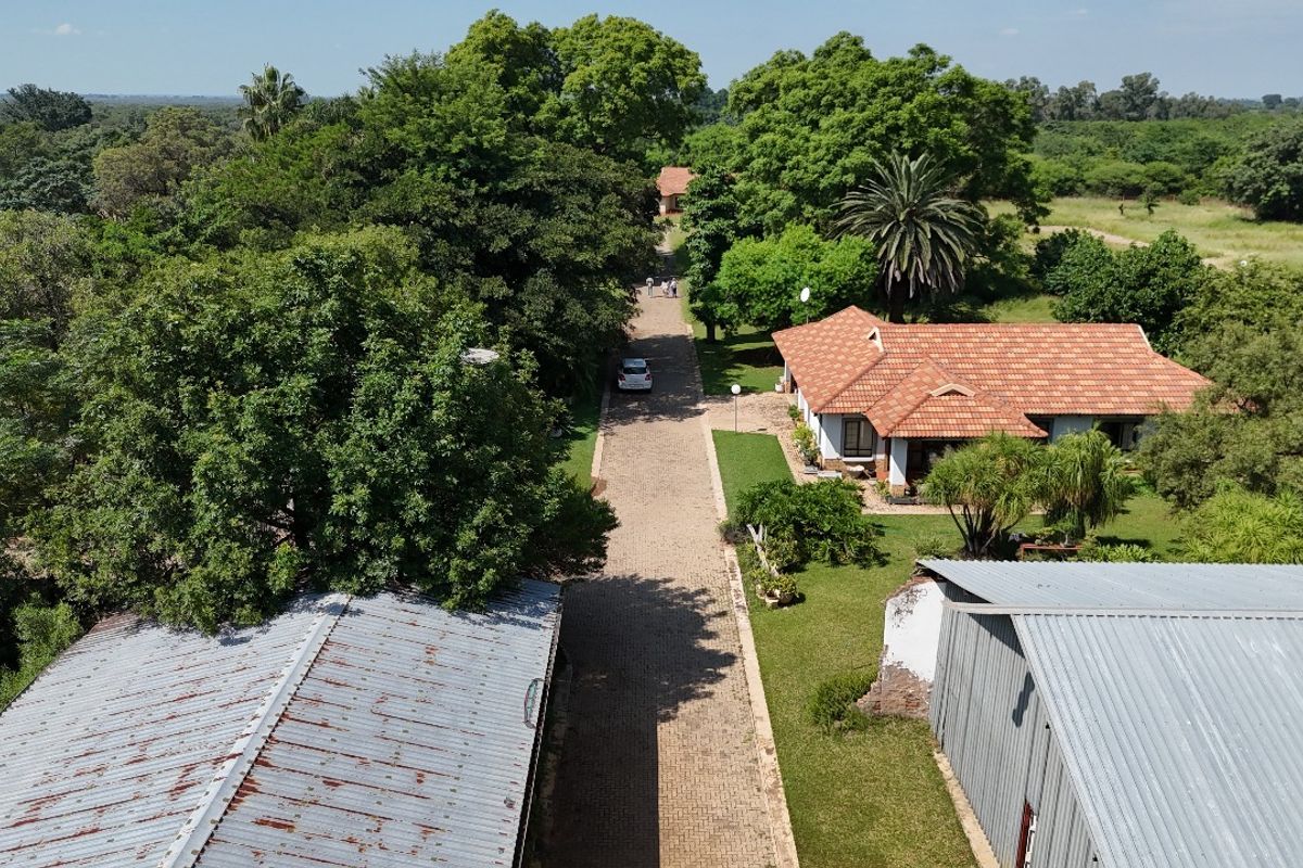 Aerial view of a residential property featuring a paved driveway, mature garden landscaping, and multiple structures with tiled and metal roofing.