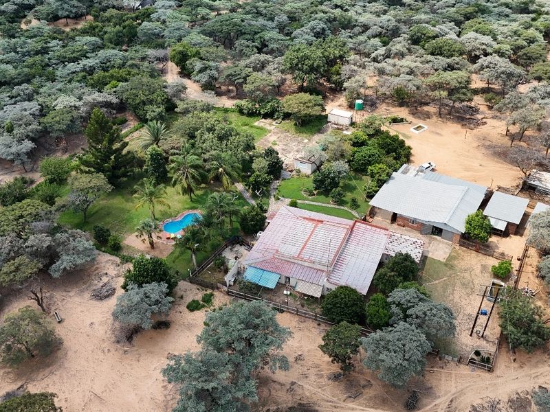 Aerial view of a small holding property featuring a main residence, swimming pool, outbuildings, and extensive surrounding natural landscape.