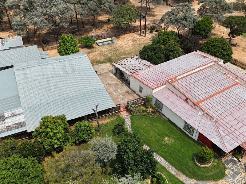 Aerial view of the small holding property featuring multiple structures with corrugated metal roofing, established garden areas, and paved pathways.