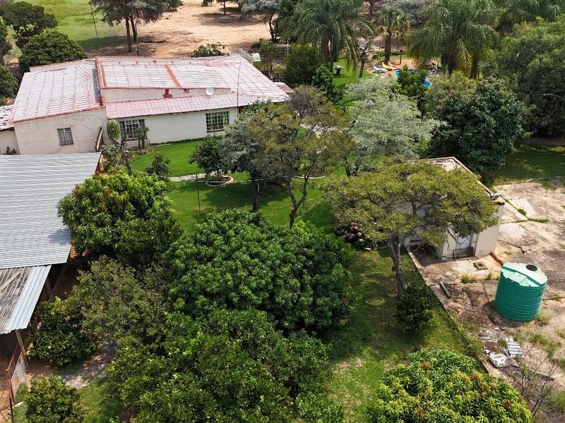 Aerial view of a small holding property featuring multiple roof structures, a large garden, and a water storage tank on a concrete area.