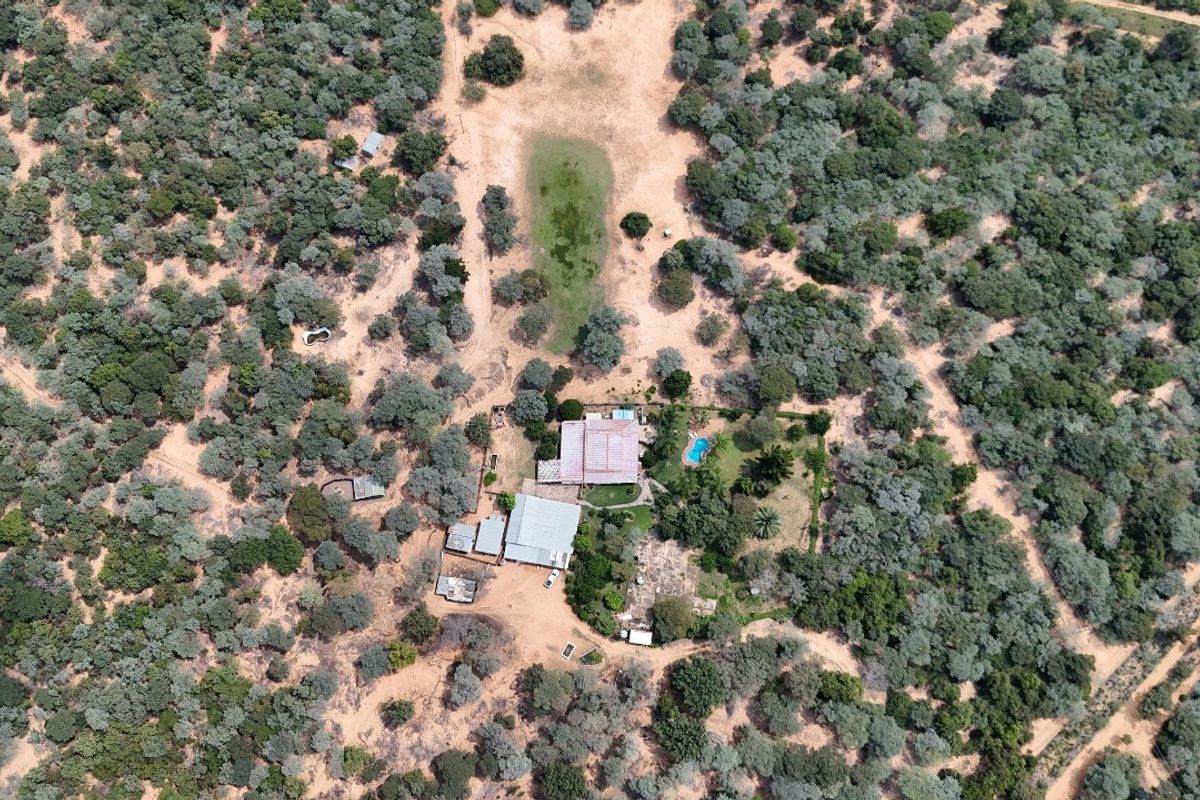 Aerial view of a small holding property featuring a main dwelling with a metal roof, a swimming pool, and surrounding natural bushveld landscape.