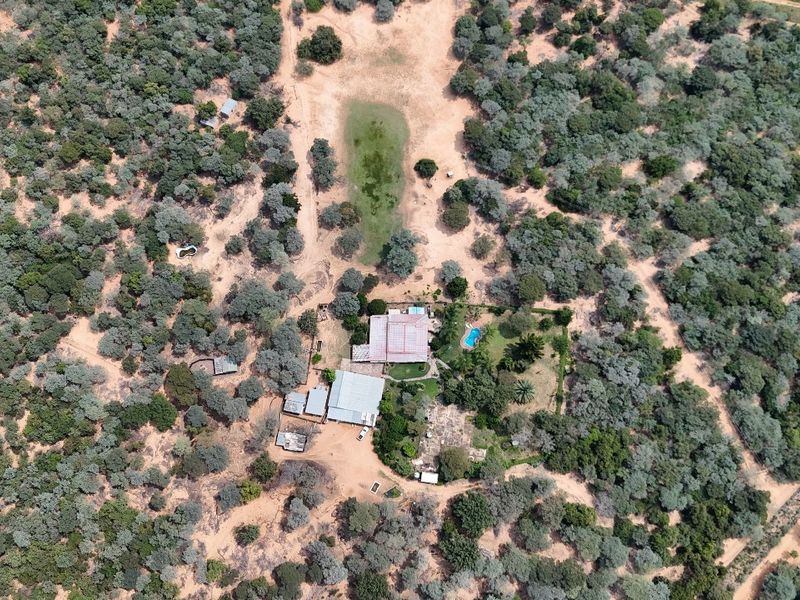 Aerial view of a small holding property featuring a main dwelling with a metal roof, a swimming pool, and surrounding natural bushveld landscape.