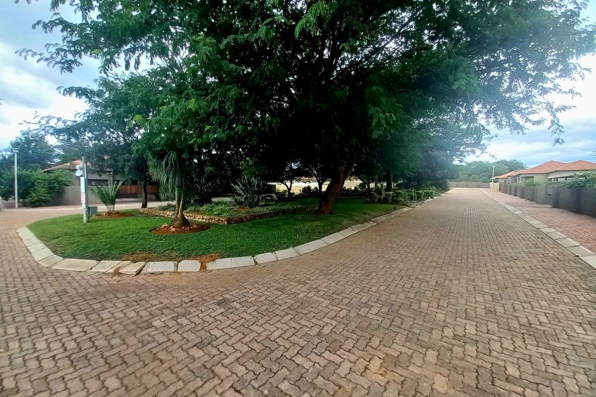 A view of the paved residential street and driveway, featuring mature trees and well-maintained landscaped garden areas within the estate.
