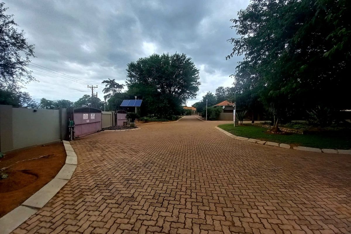 A view of a paved residential driveway leading into the property, featuring perimeter walling, security gate access, and established trees.