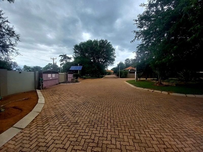 A view of a paved residential driveway leading into the property, featuring perimeter walling, security gate access, and established trees.