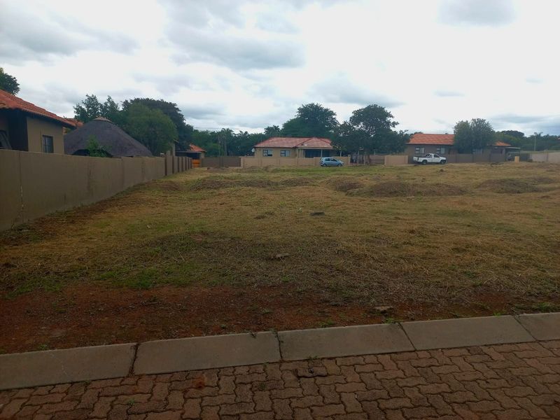 A vacant residential plot featuring a perimeter wall and paved verge, offering a clear space for future development.