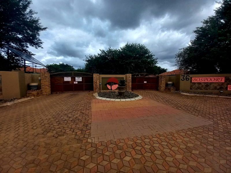 Front entrance view of the property featuring a paved driveway, secure gated access, and perimeter walling with stone cladding details.