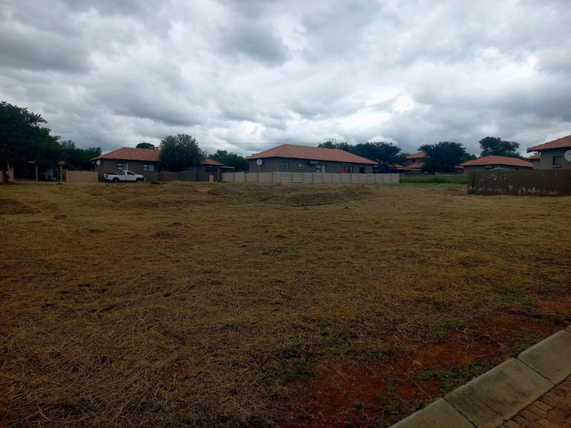 A vacant residential plot featuring cleared grass and a precast concrete boundary wall, situated in a developed neighborhood.