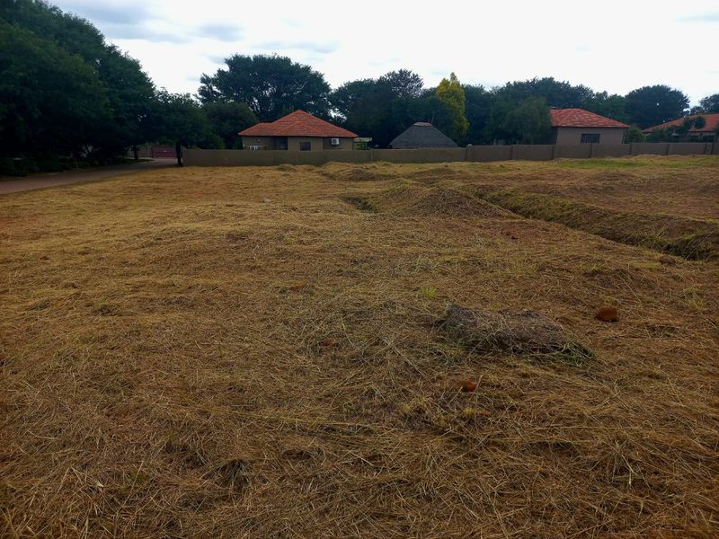 A vacant residential plot featuring cleared dry grass and a perimeter wall, offering a blank canvas for future development.