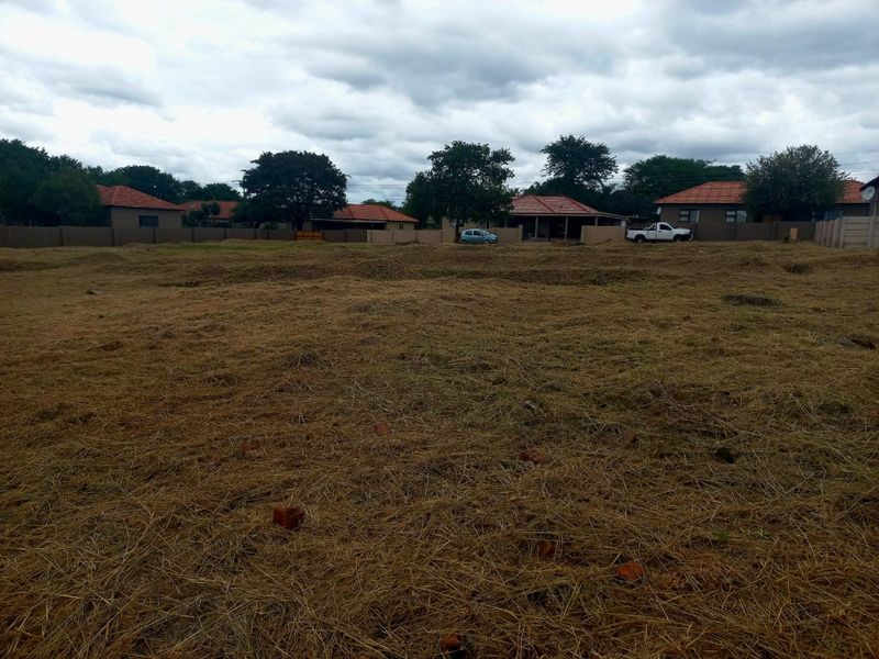 A vacant residential plot of land featuring cleared grass and perimeter walling, situated in a developed neighborhood.